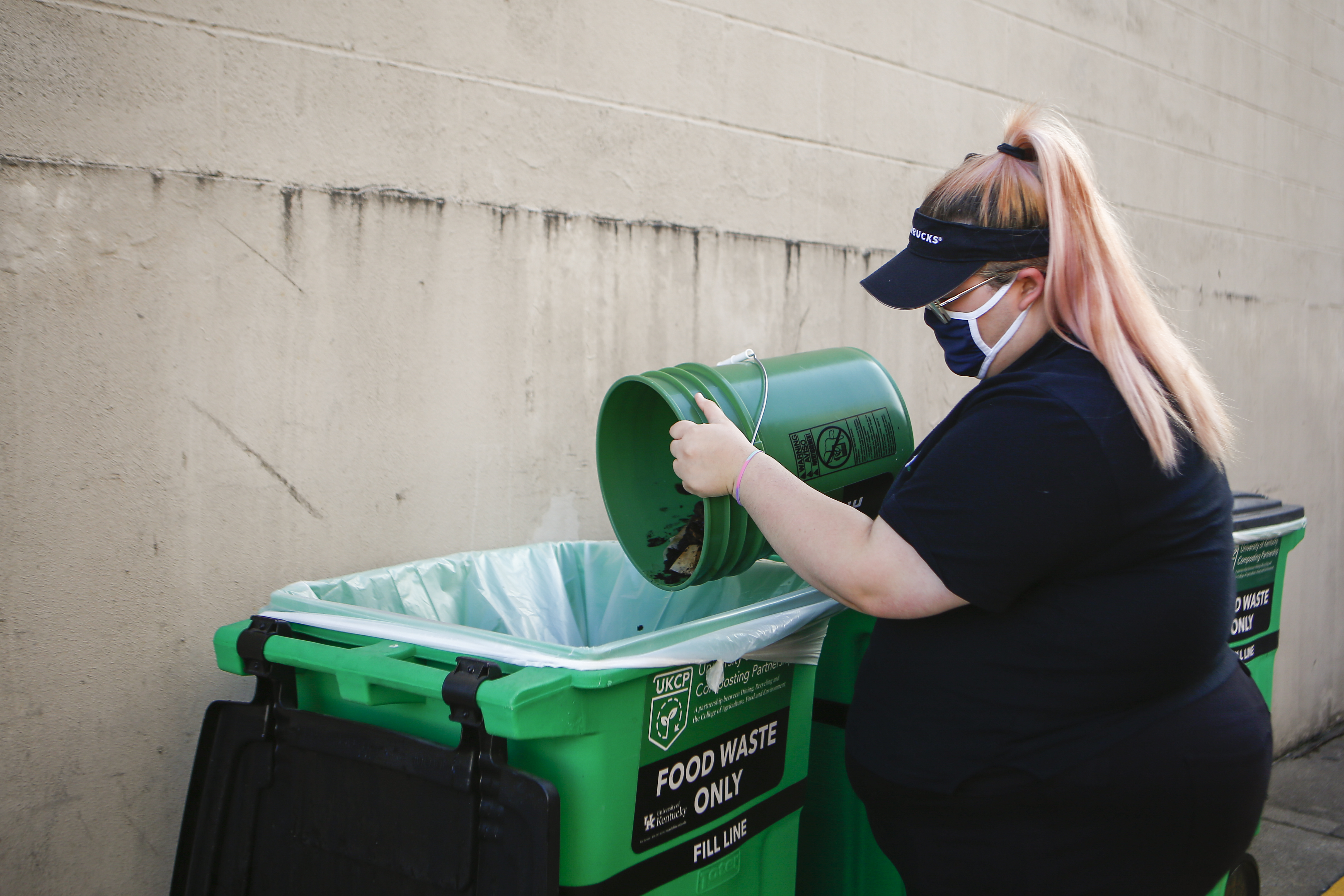 Starbucks employee empty coffee grounds into the food waste roll cart.